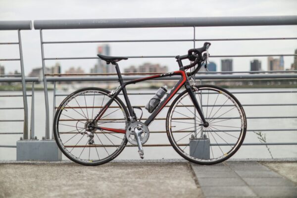 A modern road bicycle parked by the riverside railing in Taipei, with a city skyline in the background.