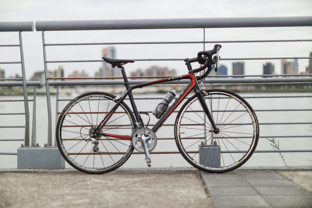 A modern road bicycle parked by the riverside railing in Taipei, with a city skyline in the background.