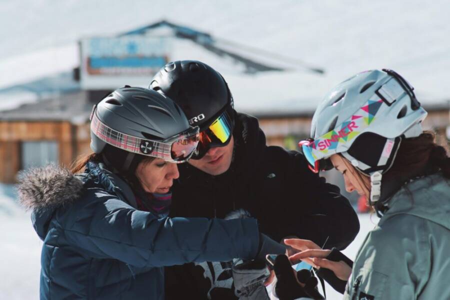 Three skiers interacting with a smartphone outdoors in Soelden, Austria during winter.