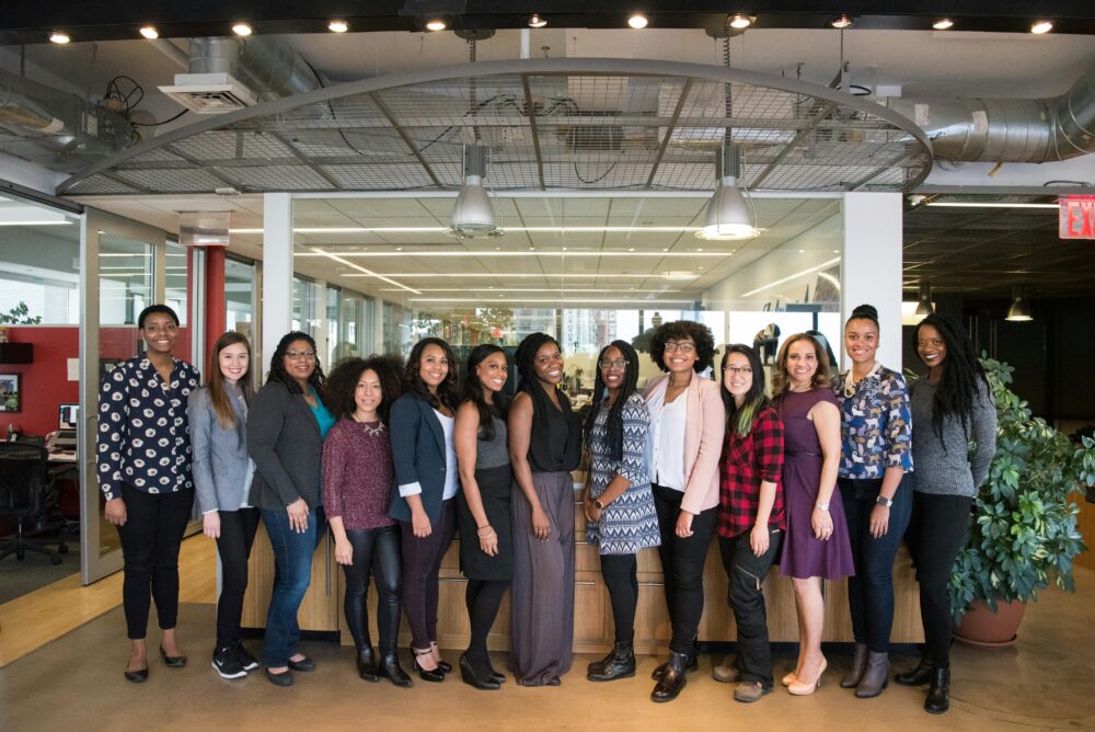 A diverse group of women in technology poses together in an office lobby, exuding confidence and teamwork