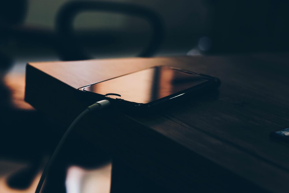 A smartphone connected to a charger lying on a wooden table indoors
