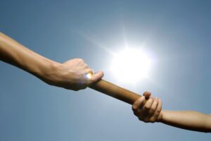 Close-up of hands passing a relay baton against a bright sunny sky