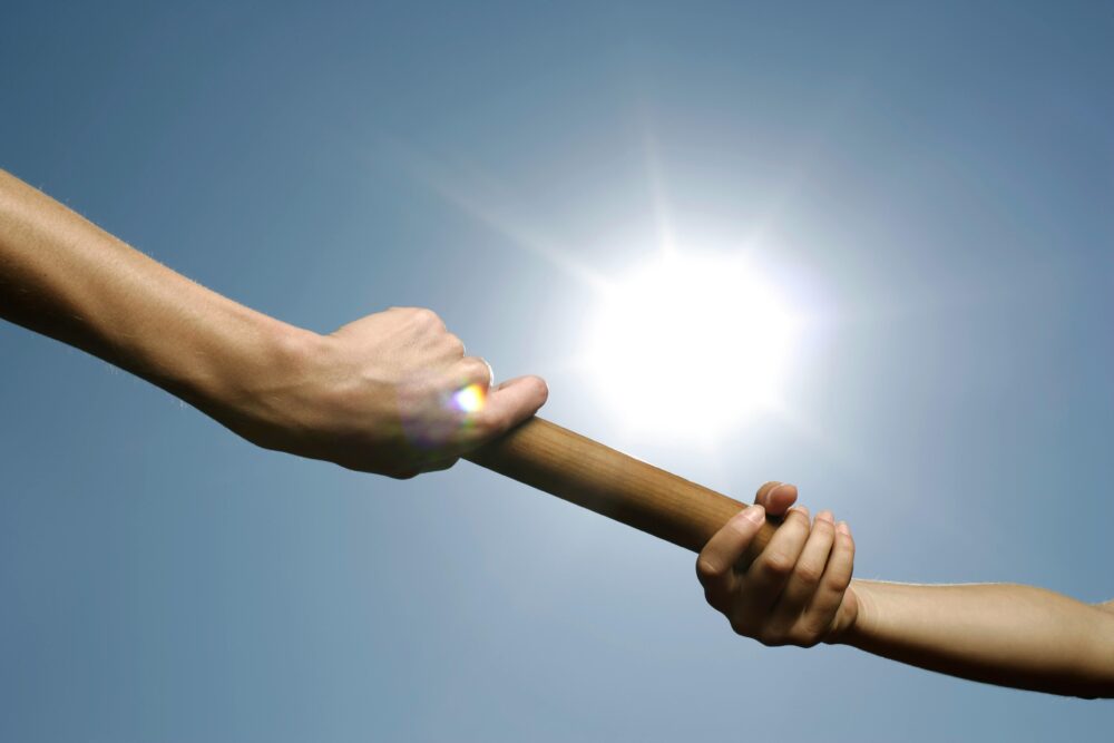 Close-up of hands passing a relay baton against a bright sunny sky