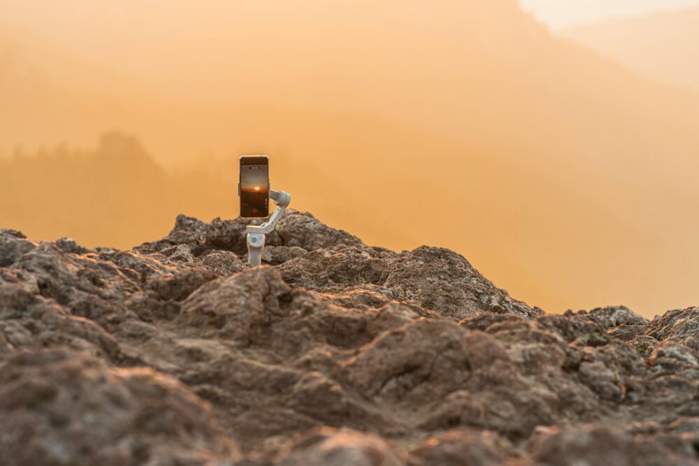Smartphone on a stabilizer capturing a stunning sunset over rocky landscape, showcasing mobile photography.
