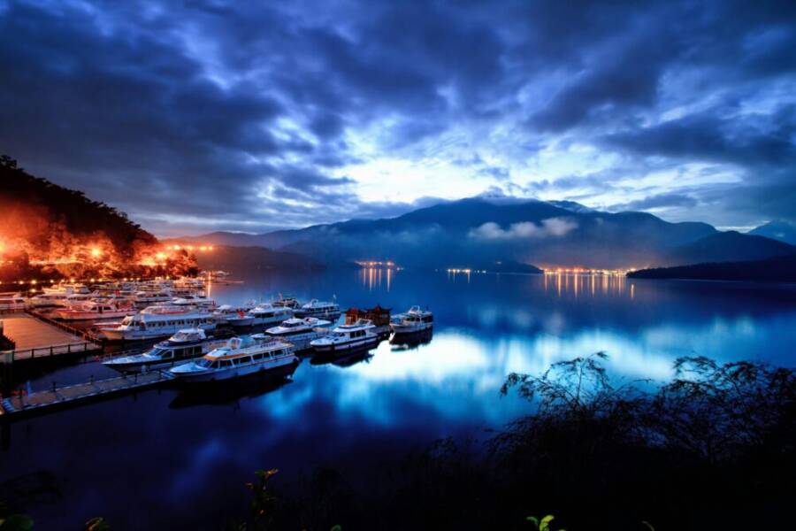 Tranquil evening at Sun Moon Lake with boats docked, surrounded by misty mountains.