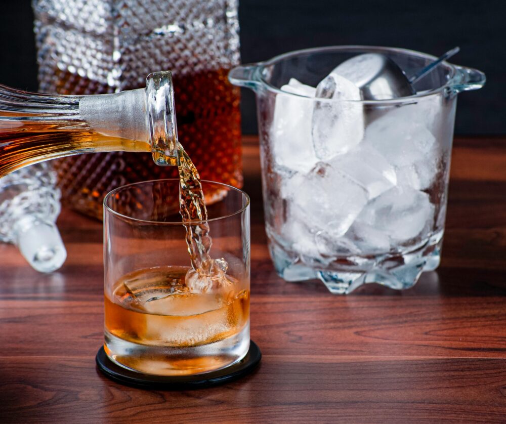 A close-up of whiskey being poured into a glass with ice