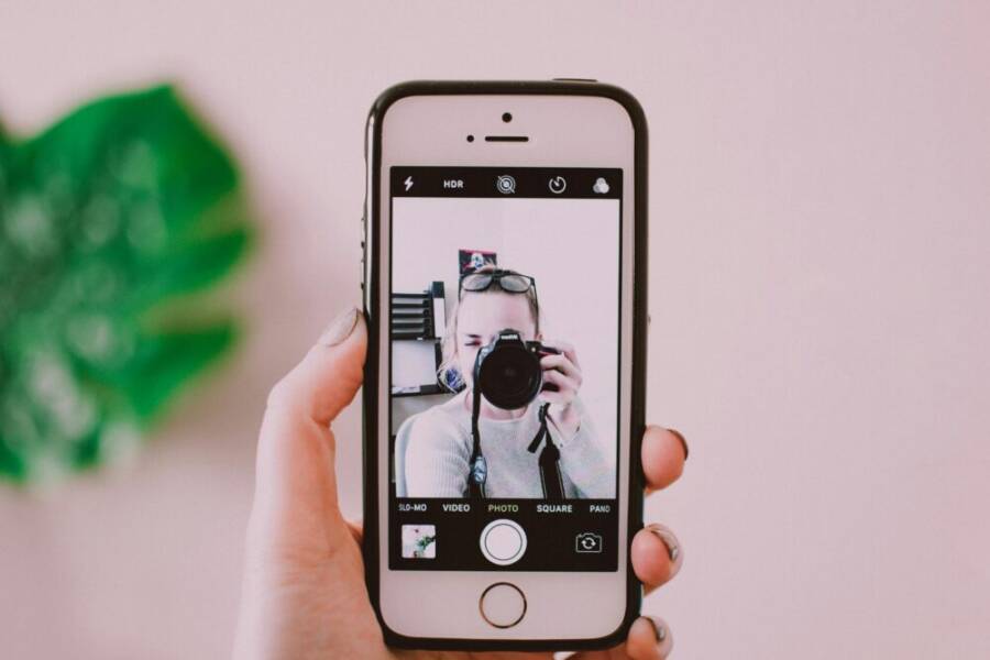 A person taking a selfie with a camera through a smartphone, showing a creative reflection