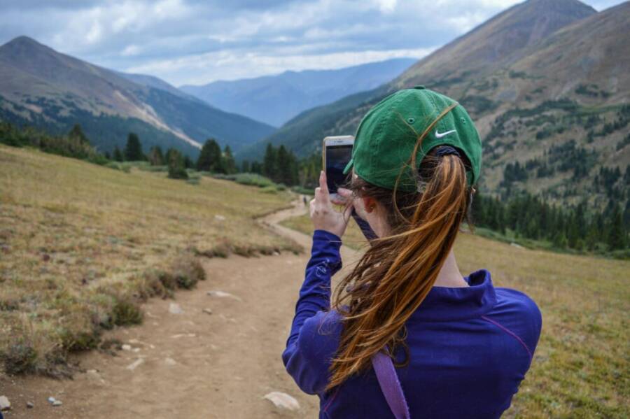 Woman capturing scenic mountain view with smartphone while hiking on a trail