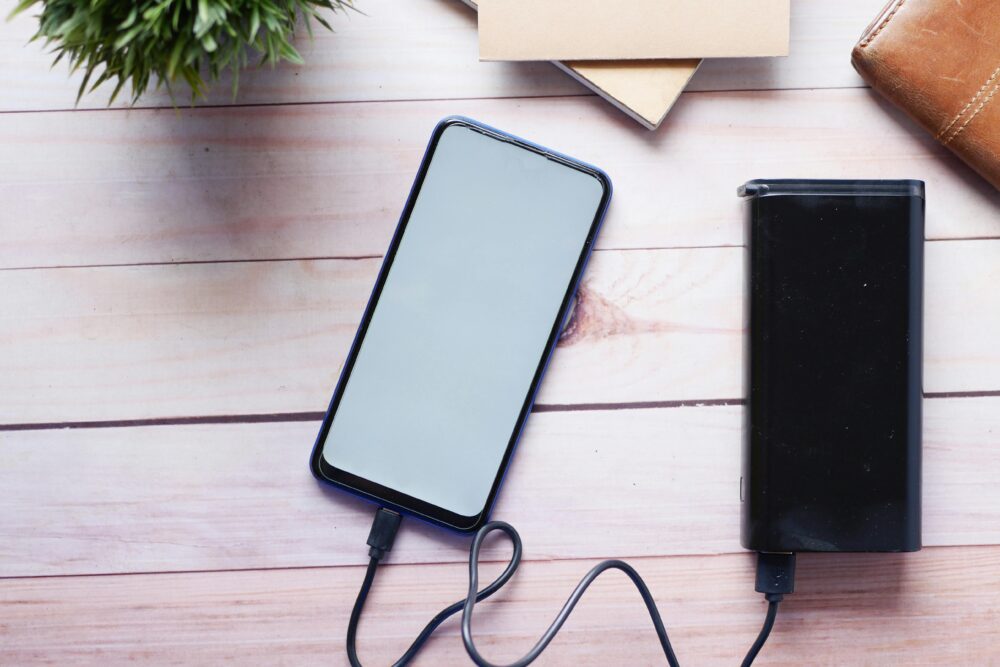 Smartphone charging with a power bank on a wooden desk, showcasing modern technology essentials.
