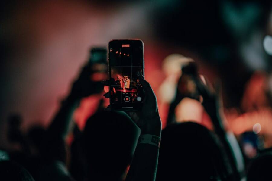 A close-up of a smartphone recording a lively concert scene with colorful stage lights.