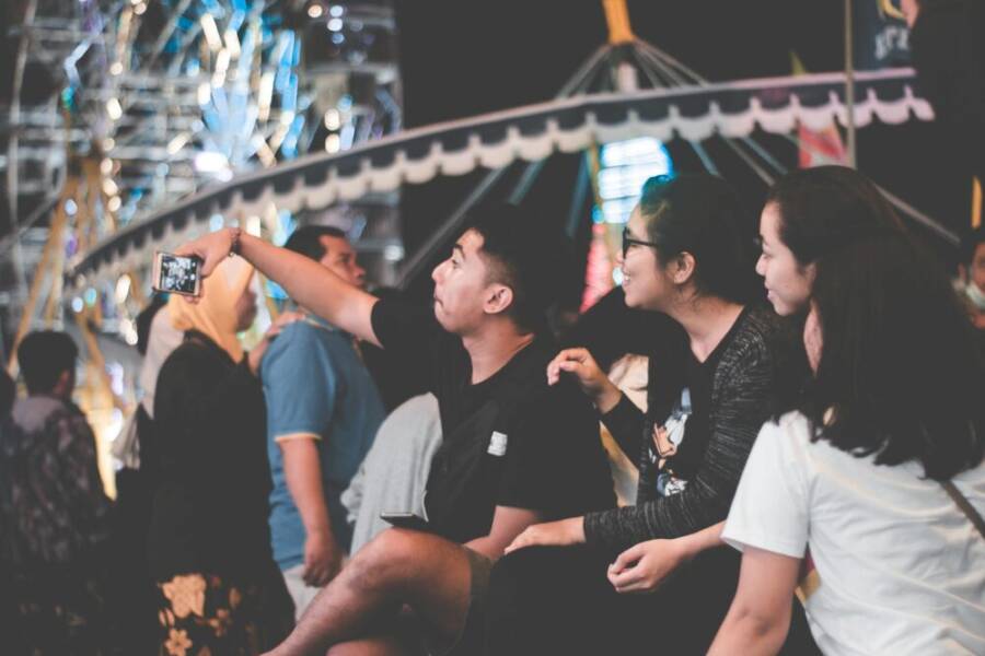 Group of friends taking selfies at a vibrant nighttime carnival.