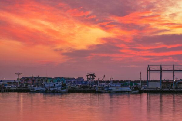 Captivating sunset view over fishing boats and colorful buildings in a Taiwan harbor, capturing the serene beauty of the scene.