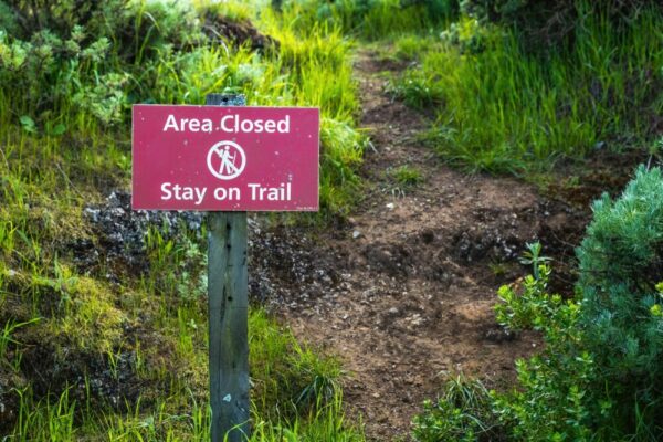 A trail sign warns hikers to stay on the designated path and alerts of closed areas.