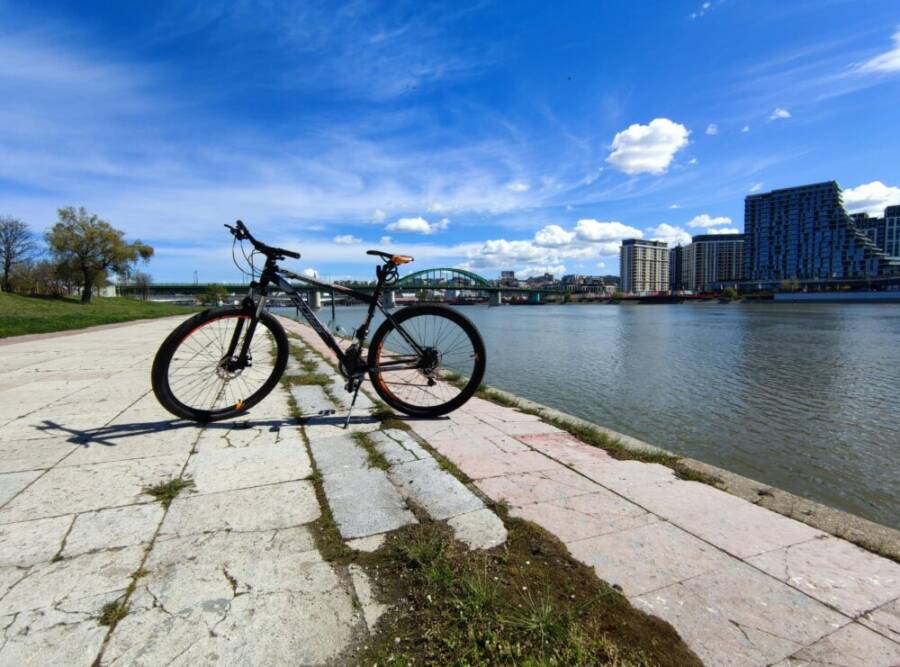 Bicycle parked on a riverside walkway with modern urban architecture under a bright blue sky