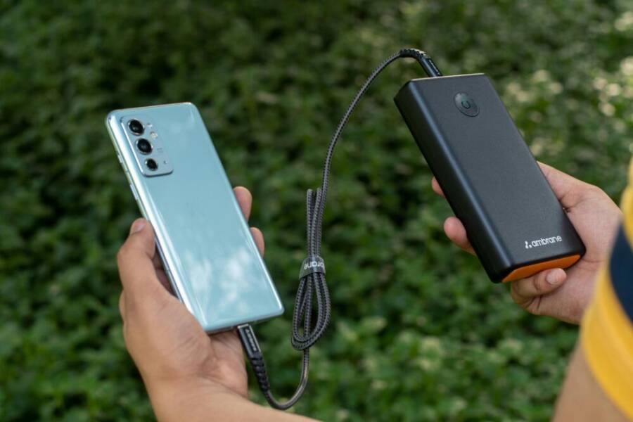 Hands holding a smartphone and powerbank connected by cable, outdoors setting