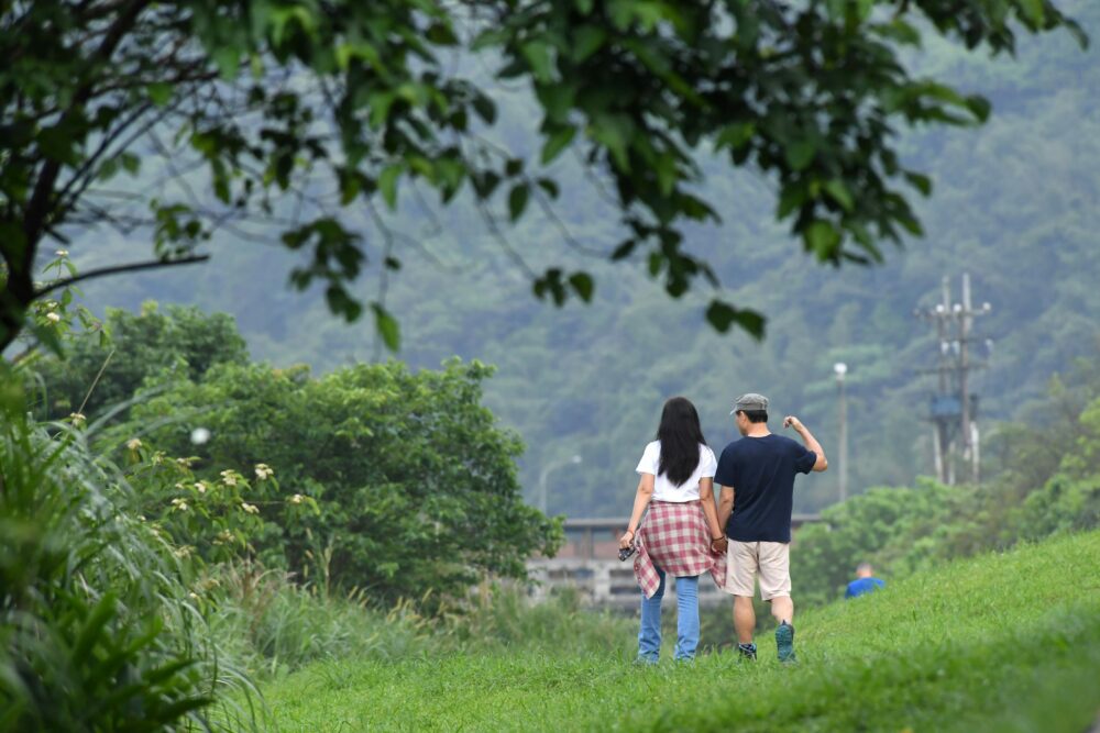 A couple walks hand in hand through a lush green landscape in Nuannuan District, Taiwan.