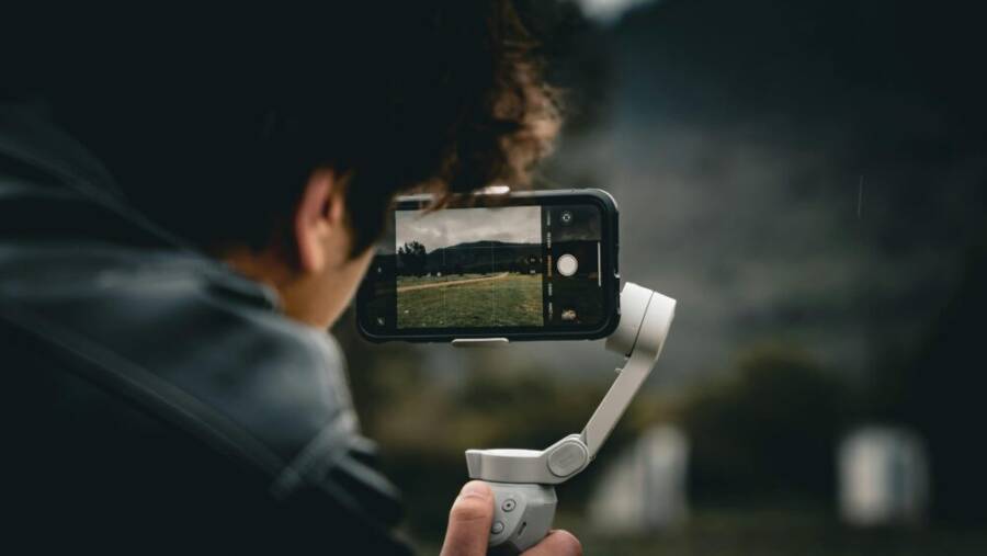 Person using a smartphone and gimbal to film a scenic outdoor landscape