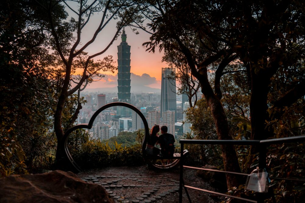 A couple sits on a scenic hill, admiring Taipei 101 at sunset