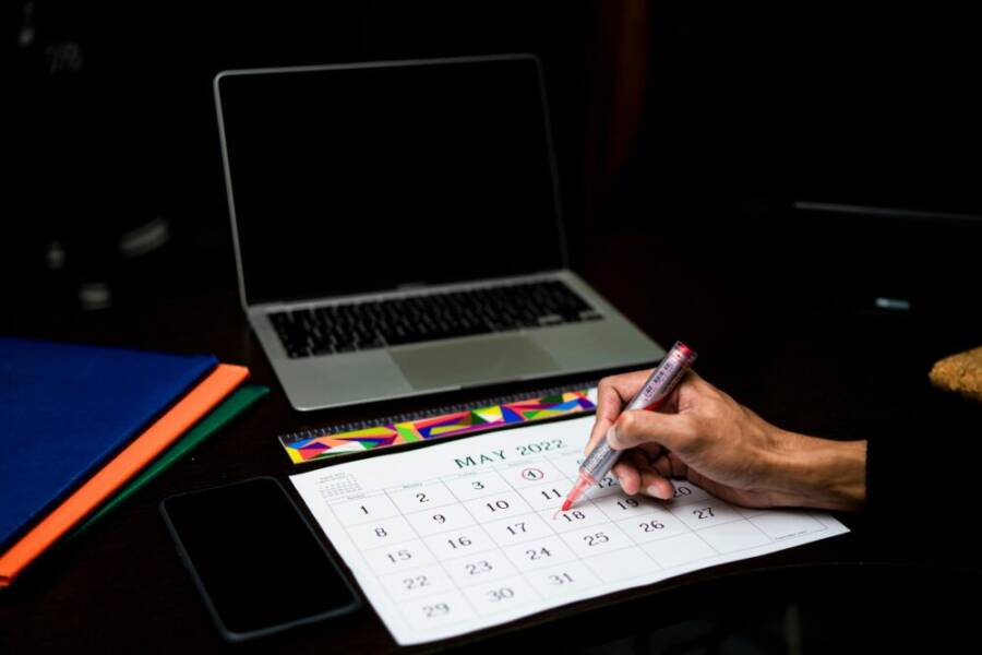 A person plans on a calendar at a desk with a laptop and phone, May 2022