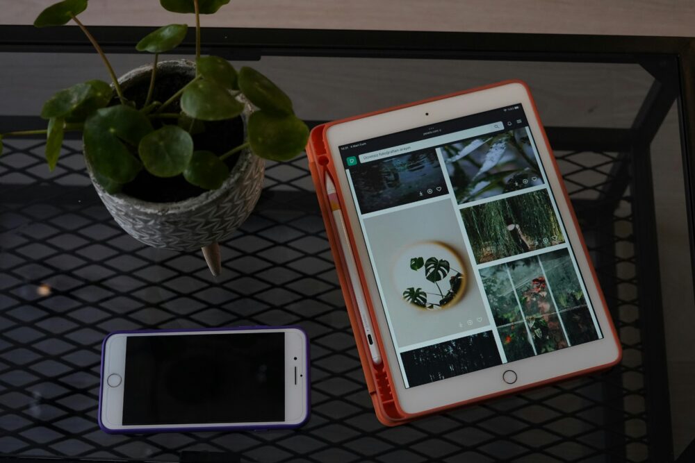 A tablet and smartphone on a metal desk next to a potted plant, showcasing modern technology.