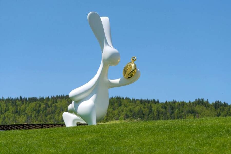 Sculpture of a white rabbit with a clock in a Swiss meadow under blue skies.