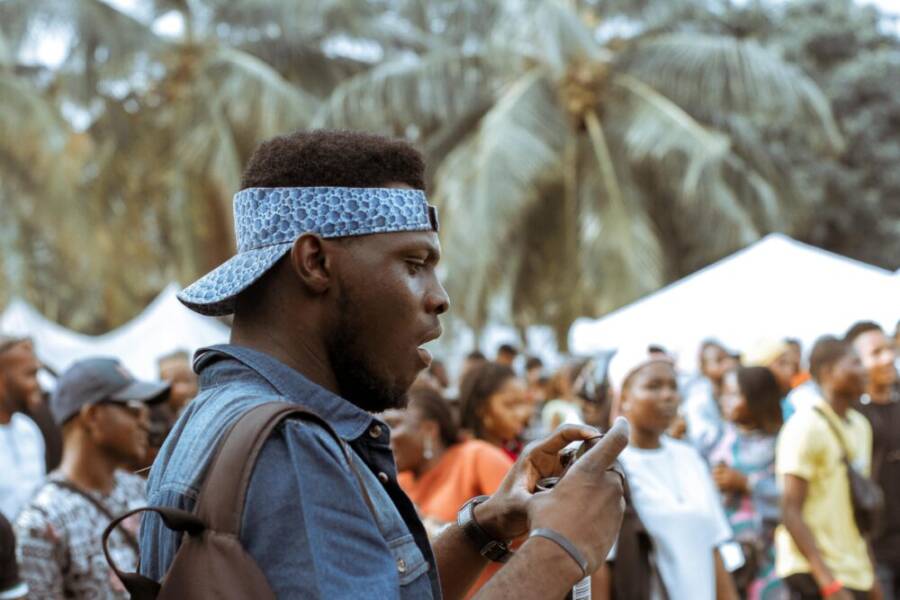 A young man in a vibrant street festival captures moments with his phone.