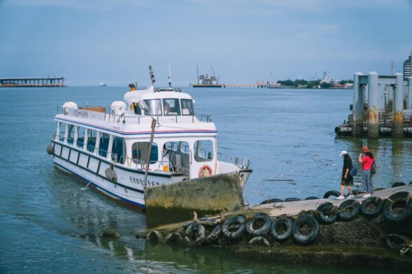 A ferry docked at a shore in New Taipei City, Taiwan, with people strolling by the sea.