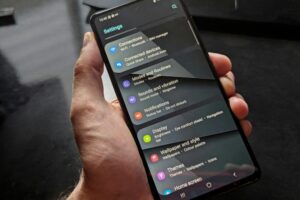 Hand holding smartphone displaying settings screen with various options evident.