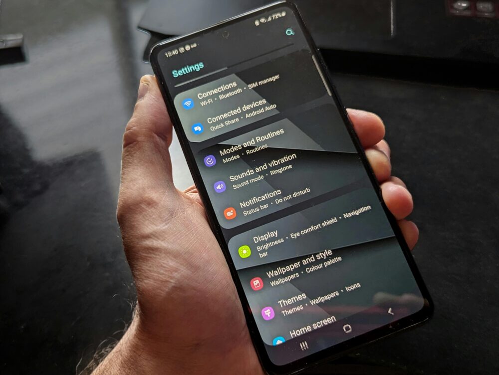 Hand holding smartphone displaying settings screen with various options evident.