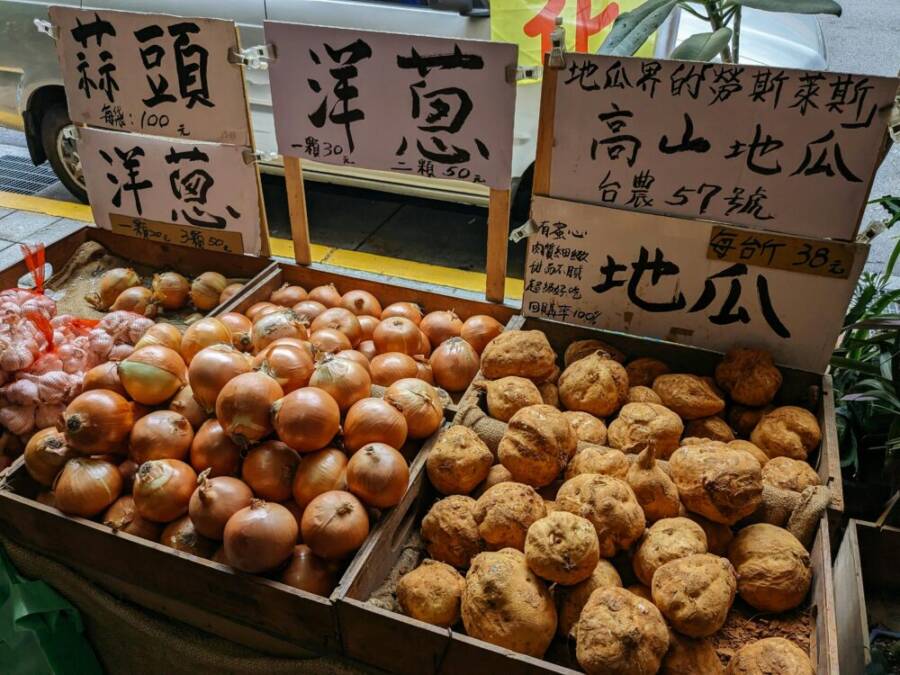 Onions and root vegetables artfully arranged in wooden crates at a Taiwanese market stall