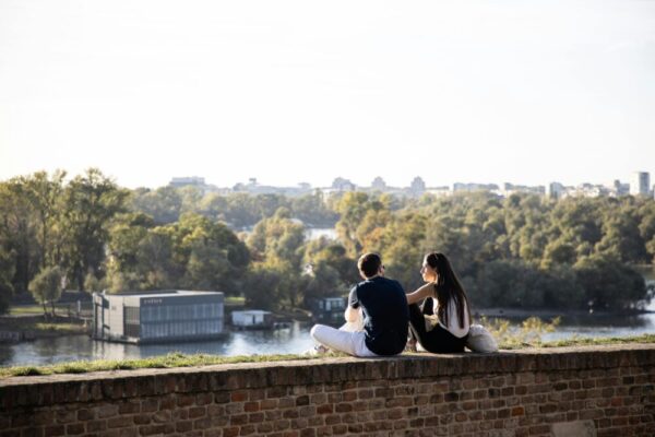 A couple sitting on a brick wall overlooking a scenic urban river landscape