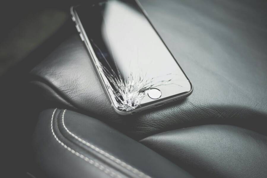 Close-up of a broken smartphone with a cracked screen on a leather car seat