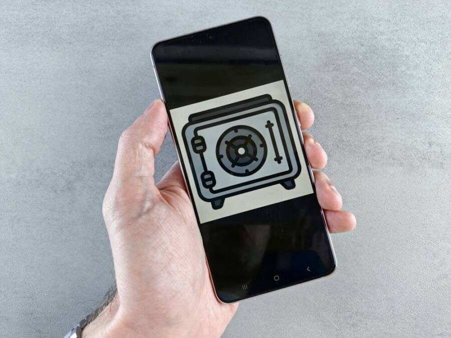 Close-up of a smartphone showing a safe icon held in a hand, symbolizing digital security