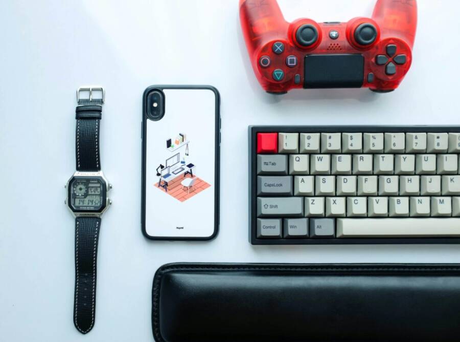 Top view of modern gadgets including a smartphone, watch, game controller, and keyboard