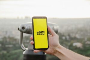 Hand holding smartphone with eSIM app, cityscape view of Los Angeles in background.