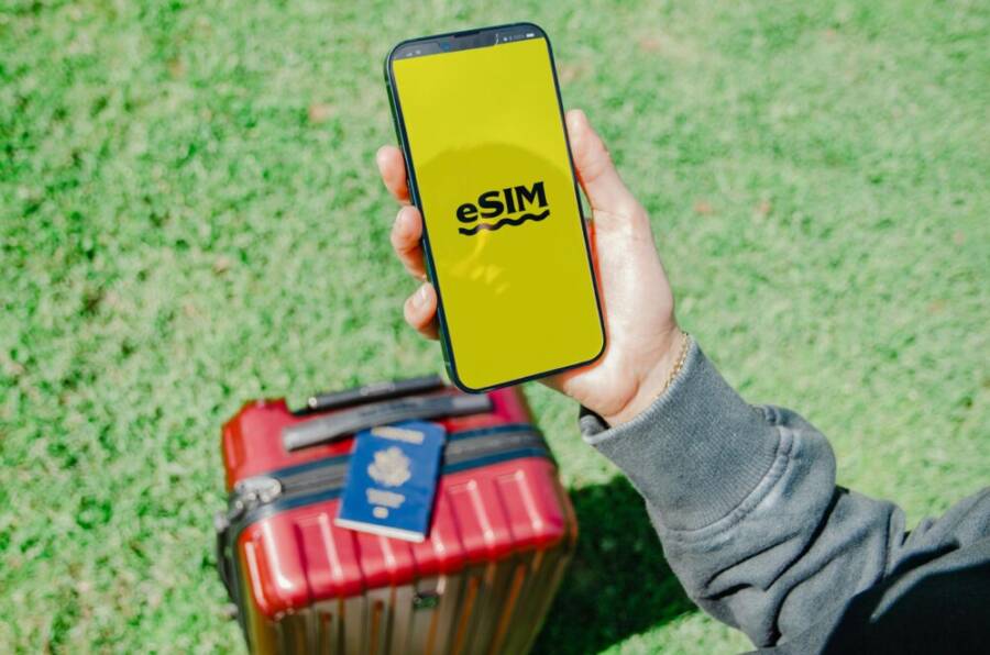 Traveler in Los Angeles holding a smartphone with eSIM near a red suitcase on grass
