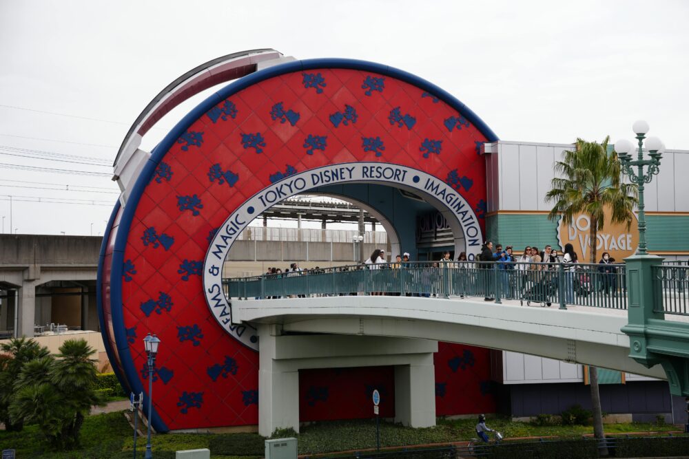 Capture of the Tokyo Disney Resort entrance featuring the Bon Voyage Store and pedestrian bridge.