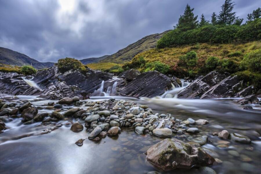 Tranquil mountain landscape with flowing waterfall and rocky stream under cloudy skies