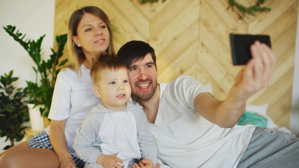 A joyful family of three enjoys a selfie moment indoors, capturing happy memories.