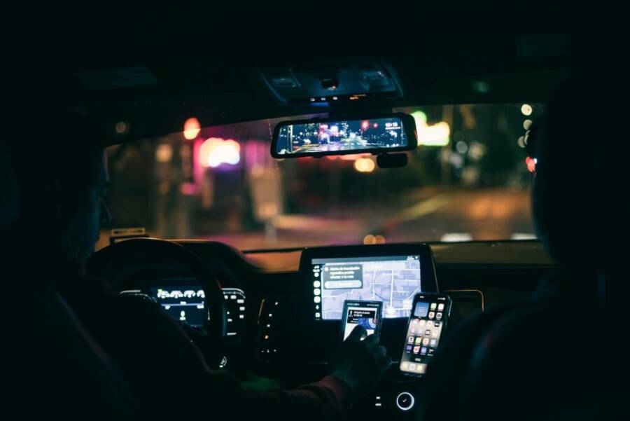 Interior view of a car at night with a driver using a smartphone for navigation through city streets