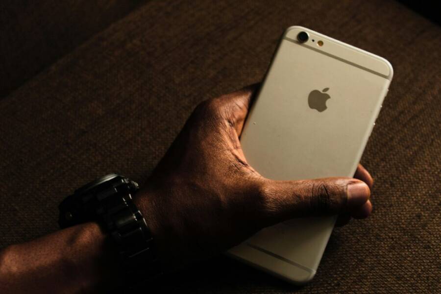Close-up of a hand holding a smartphone, wearing a wristwatch. Dark background setting.