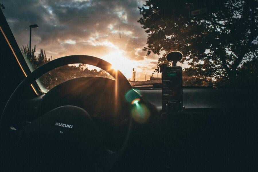 View of sunrise through a car windshield with steering wheel and smartphone visible.