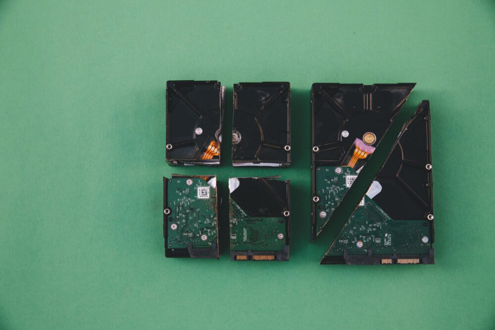 Four broken hard drives arranged on a green background, showcasing data destruction.