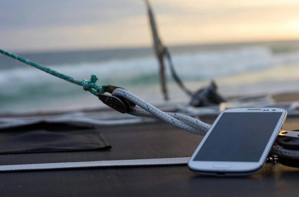Close-up of a smartphone resting on a sailboat deck with the ocean waves in the background