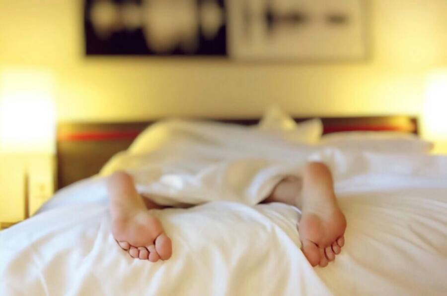 A person resting on a bed with white sheets