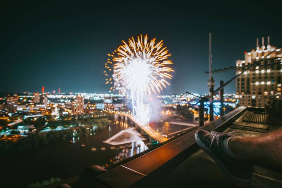 Fireworks illuminate the night sky over Minneapolis cityscape, viewed from a rooftop.