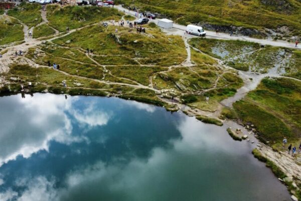 A picturesque aerial view of a serene lake surrounded by lush greenery and hiking trails reflecting the cloudy sky.