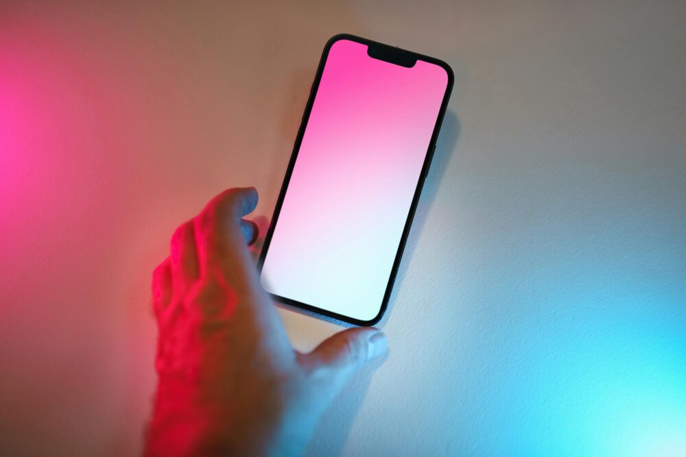 A hand reaches for a smartphone with a colorful gradient screen and ambient lighting.