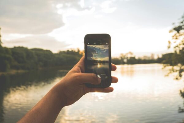 Hand photographing peaceful lake scenery with a smartphone at sunset