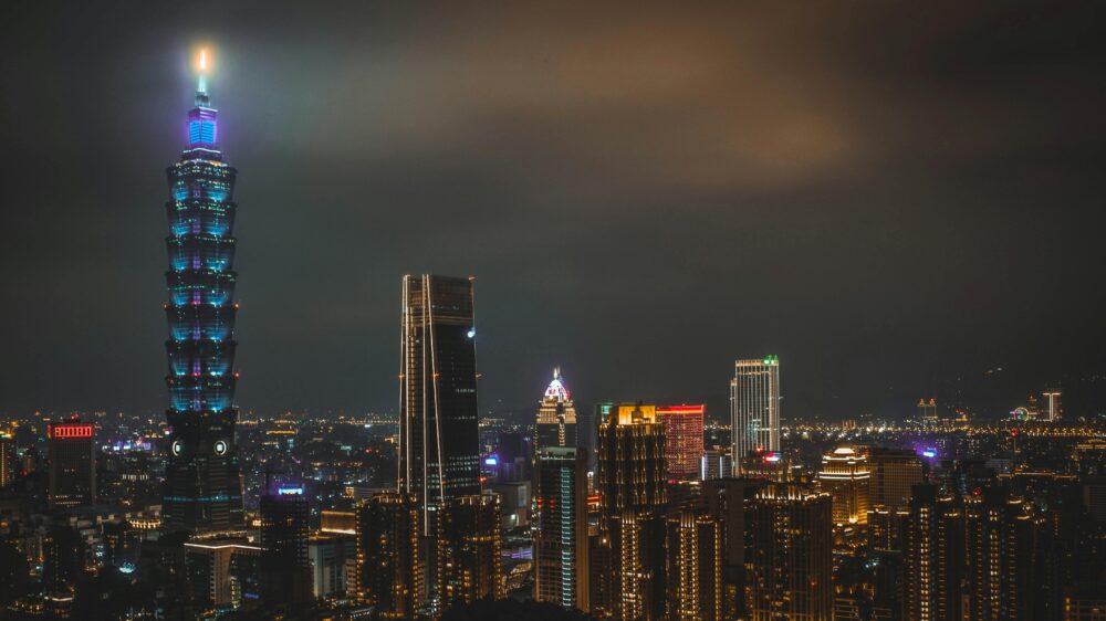 Night cityscape featuring the illuminated Taipei 101 tower and surrounding skyline in Taipei, Taiwan.